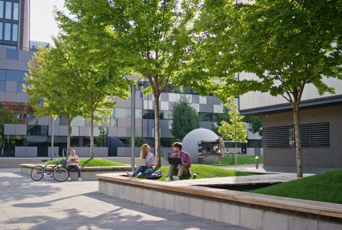 Casual people working outdoors at modern office building. Adult students study communicating in urban park. Freelancer team colleagues browsing laptop internet on sunny street. Education remote work