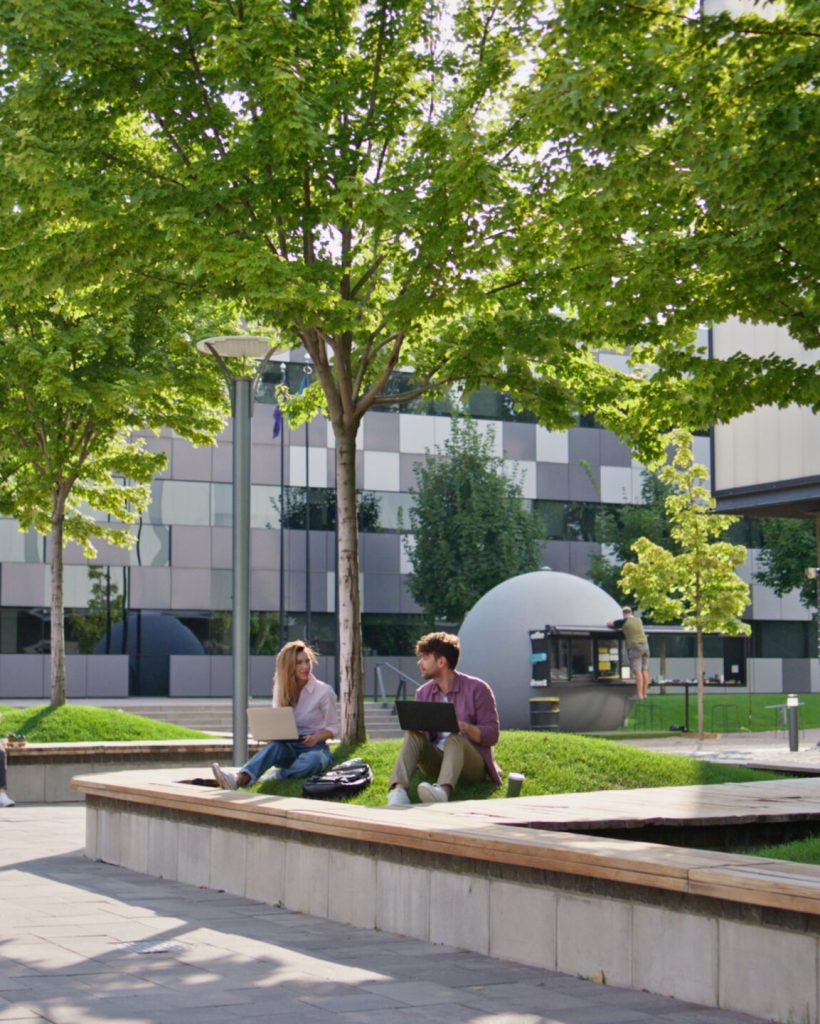 Casual people working outdoors at modern office building. Adult students study communicating in urban park. Freelancer team colleagues browsing laptop internet on sunny street. Education remote work
